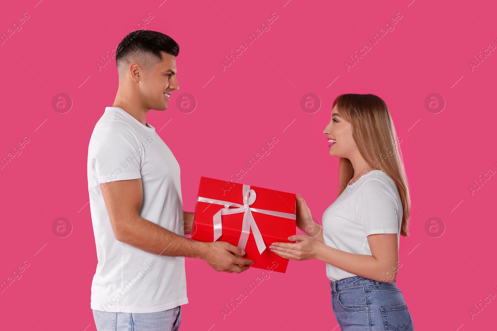 Photo of Man surprising his girlfriend with gift on pink background. Valentine's day celebration