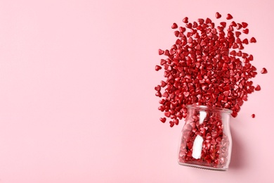 Red heart shaped sprinkles and glass jar on pink background, flat lay. Space for text