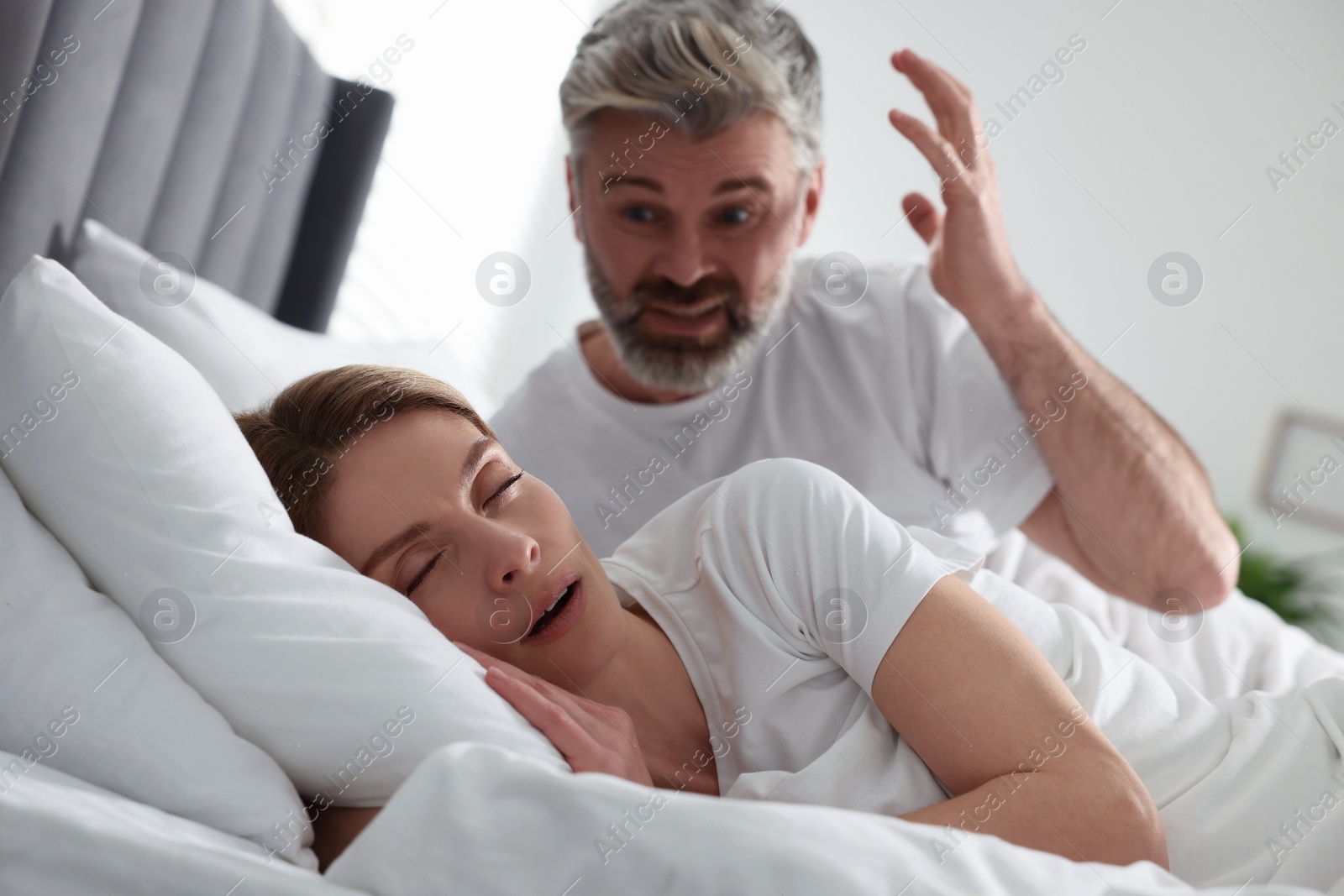 Photo of Irritated man near his snoring wife in bed at home