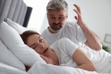 Photo of Irritated man near his snoring wife in bed at home
