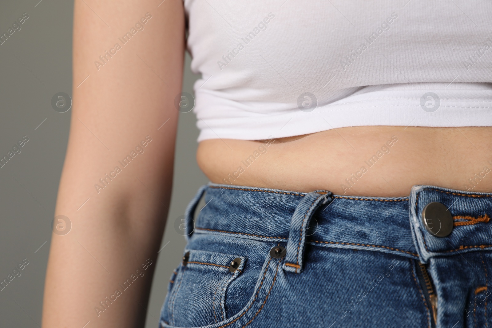 Photo of Overweight woman in tight tshirt and jeans on grey background, closeup