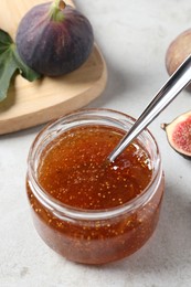 Jar with tasty fig jam and fresh fruits on white table, closeup