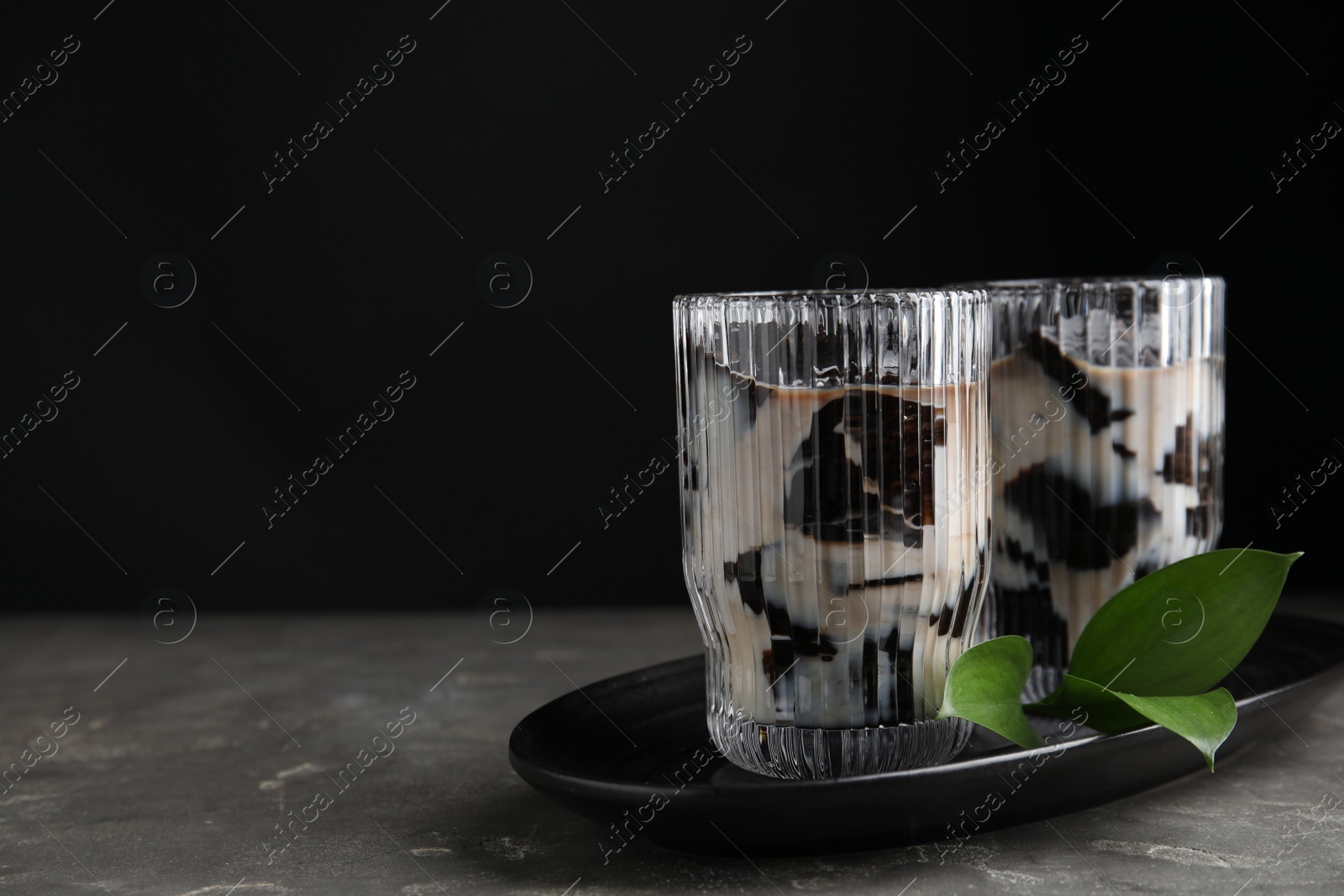 Photo of Glasses of milk with grass jelly and green leaves on grey table, space for text