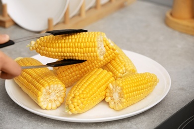 Photo of Taking corn cob from plate with tongs, closeup