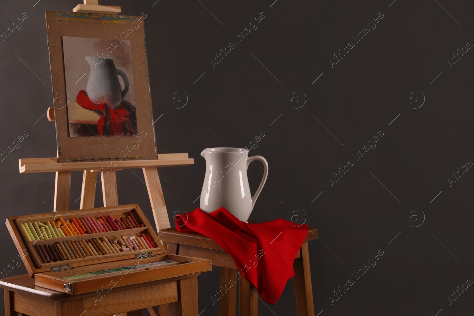 Photo of Artist's workplace with easel, drawing and soft pastels against black background, space for text