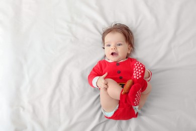 Photo of Cute baby wearing festive Christmas costume on white bedsheet, top view. Space for text