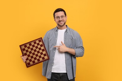Photo of Smiling man pointing at chessboard on orange background