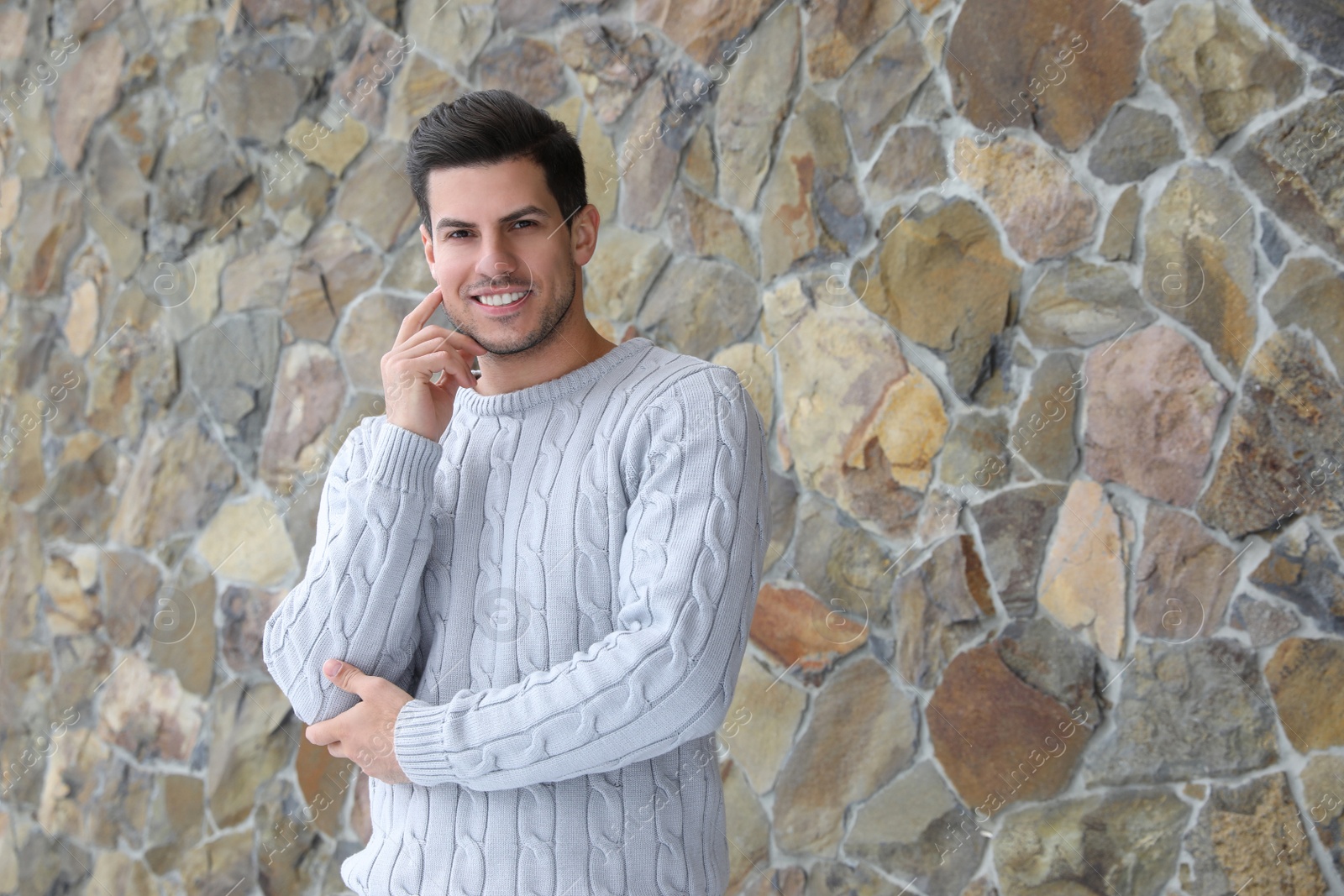 Photo of Happy man in warm sweater near stone wall. Space for text