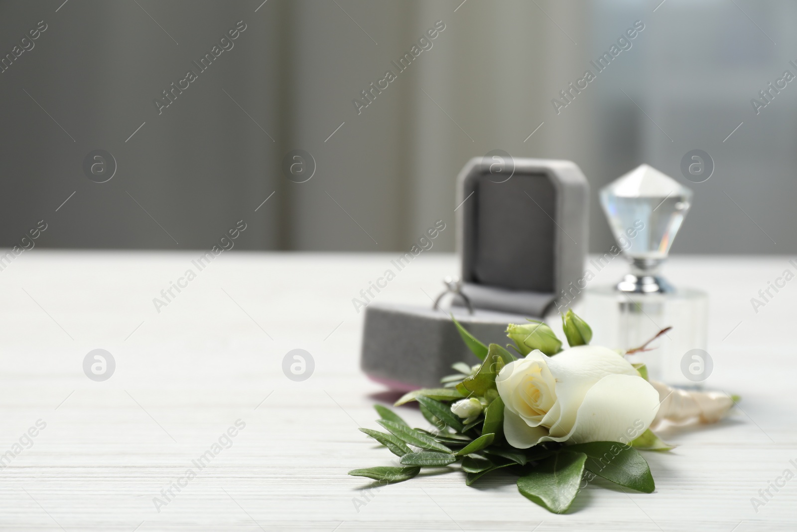 Photo of Wedding stuff. Stylish boutonniere, perfume and ring on white wooden table, closeup. Space for text