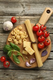 Board with different types of pasta and products on wooden table, flat lay