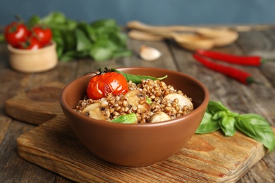 Photo of Delicious buckwheat porridge with mushrooms and tomato on wooden board