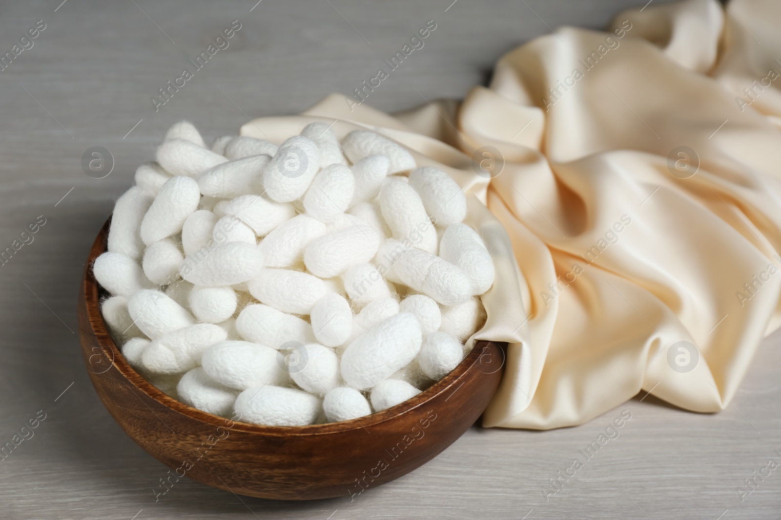 Photo of Cocoons with bowl and silk fabric on white wooden table