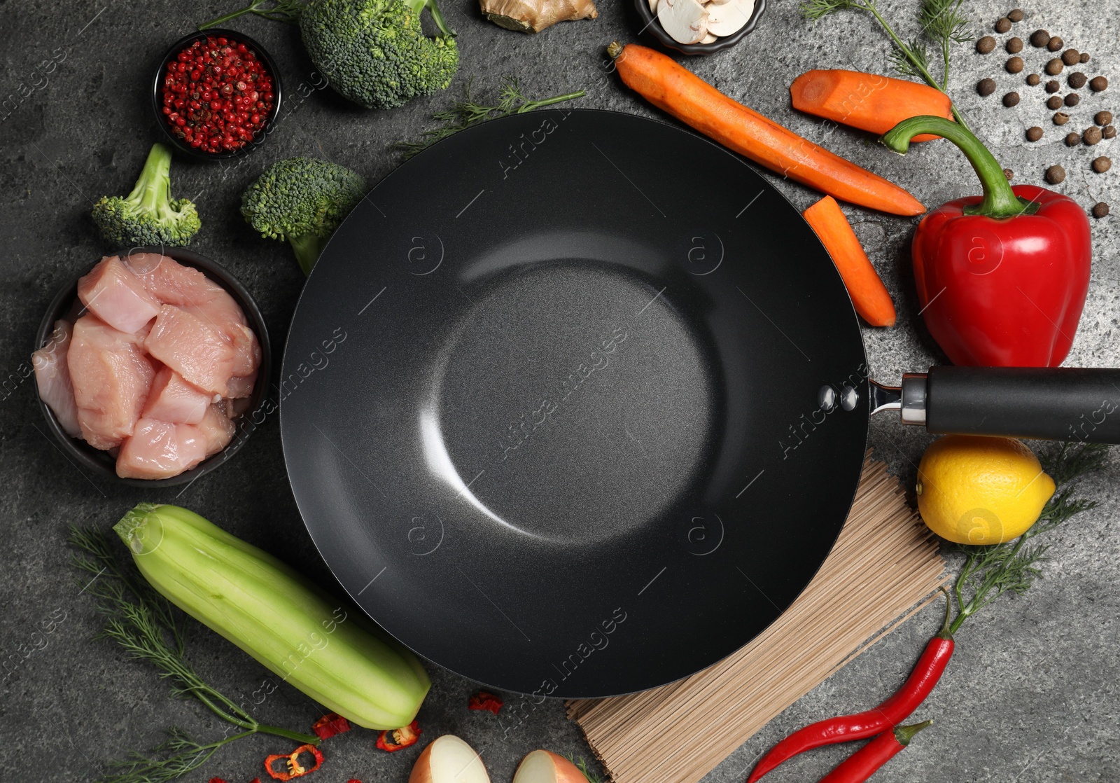 Photo of Empty iron wok surrounded by raw ingredients on grey table, flat lay