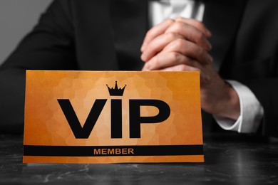 Photo of Man sitting at table with VIP sign on grey background, closeup