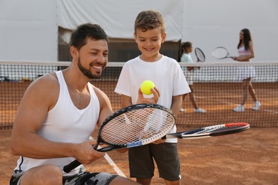 Photo of Father teaching son to play tennis on court