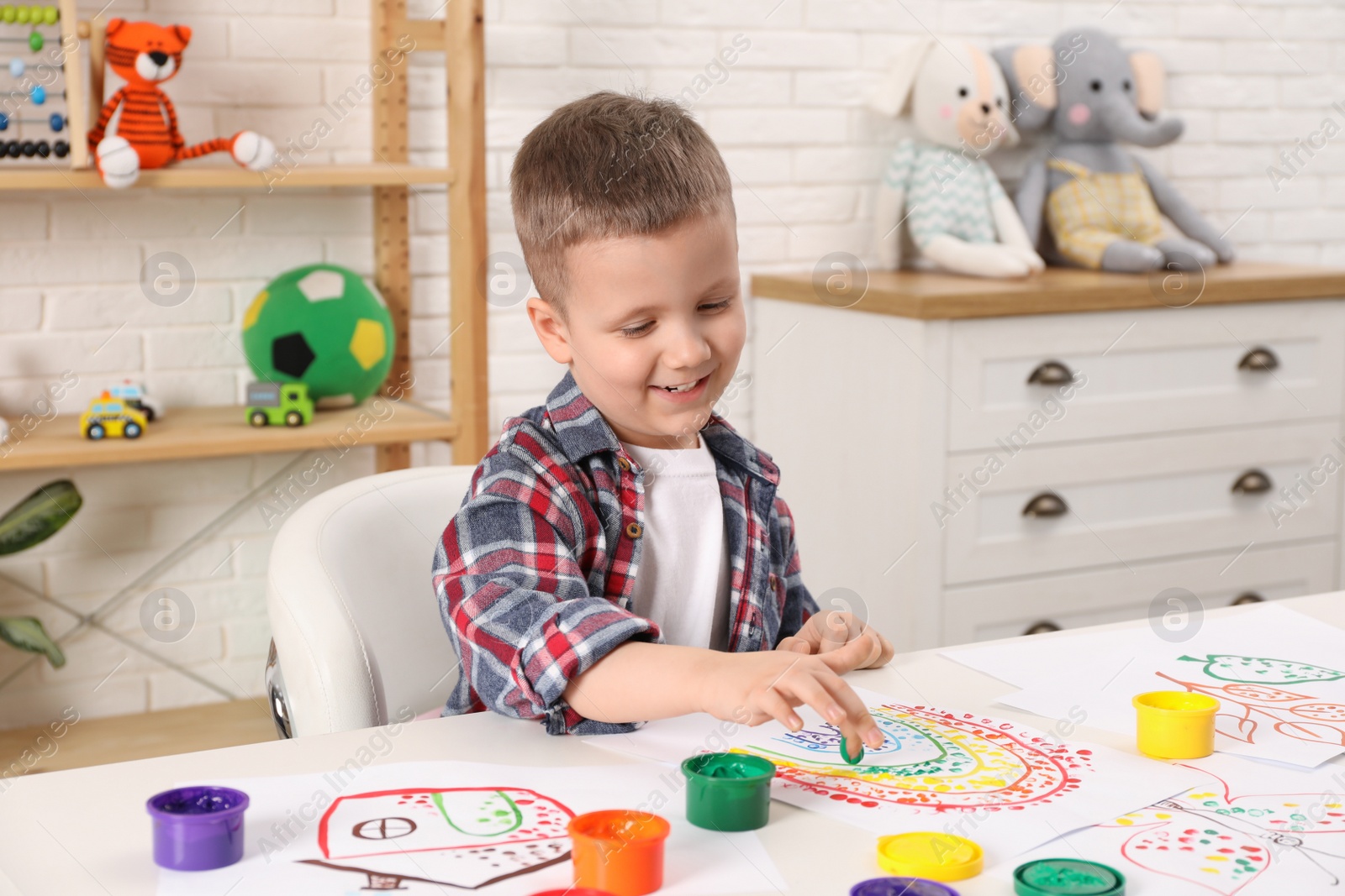 Photo of Little boy painting with finger at white table indoors