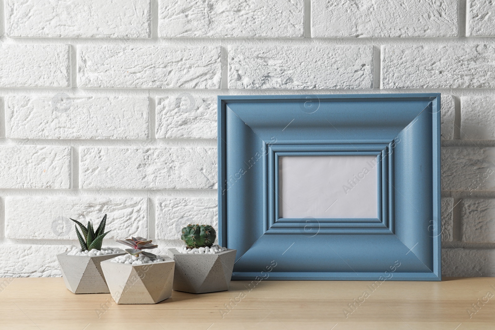 Photo of Blank frame and succulent plants on wooden table near white brick wall, space for design. Home decor