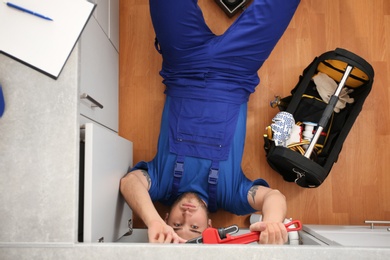 Photo of Professional plumber with set of tools working indoors, top view