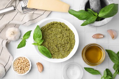 Photo of Tasty pesto sauce and ingredients on white tiled table, flat lay