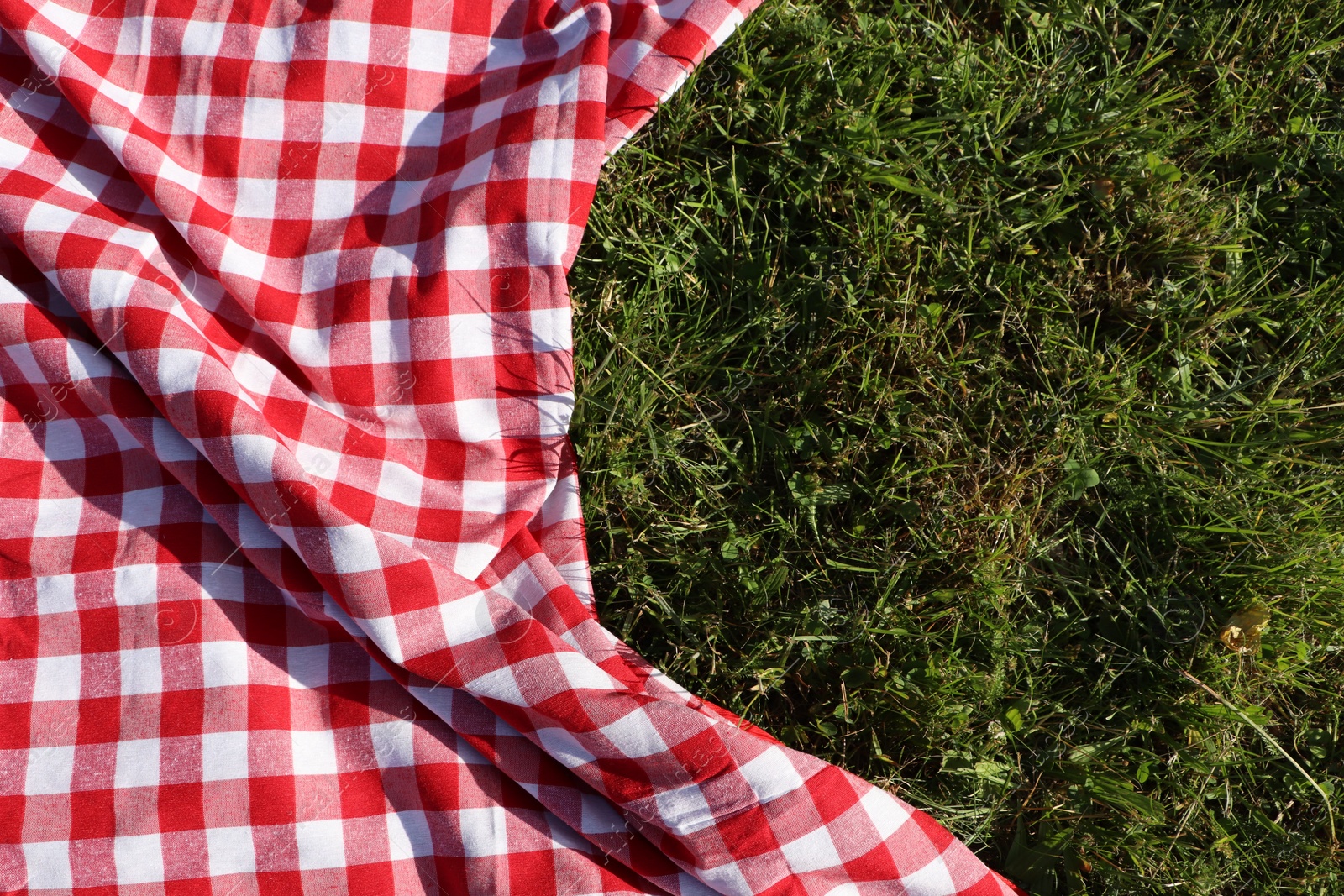 Photo of Checkered picnic tablecloth on fresh green grass, top view. Space for text