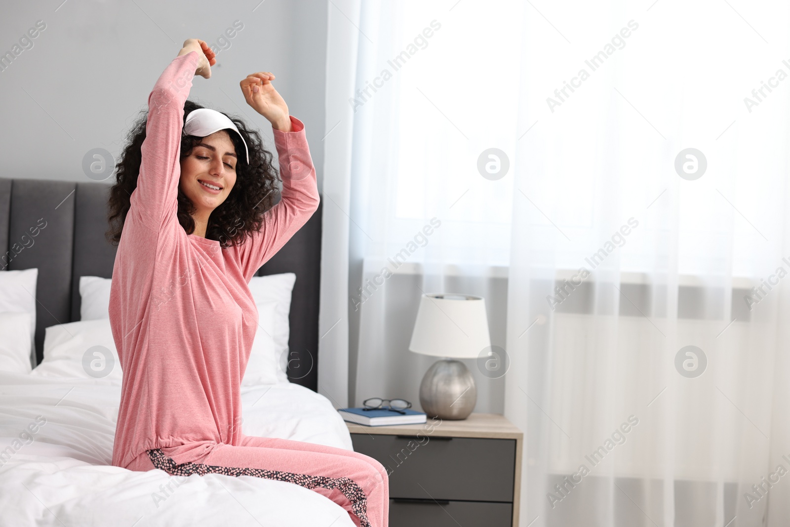 Photo of Beautiful young woman in stylish pyjama and sleep mask on bed at home, space for text