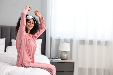 Beautiful young woman in stylish pyjama and sleep mask on bed at home, space for text