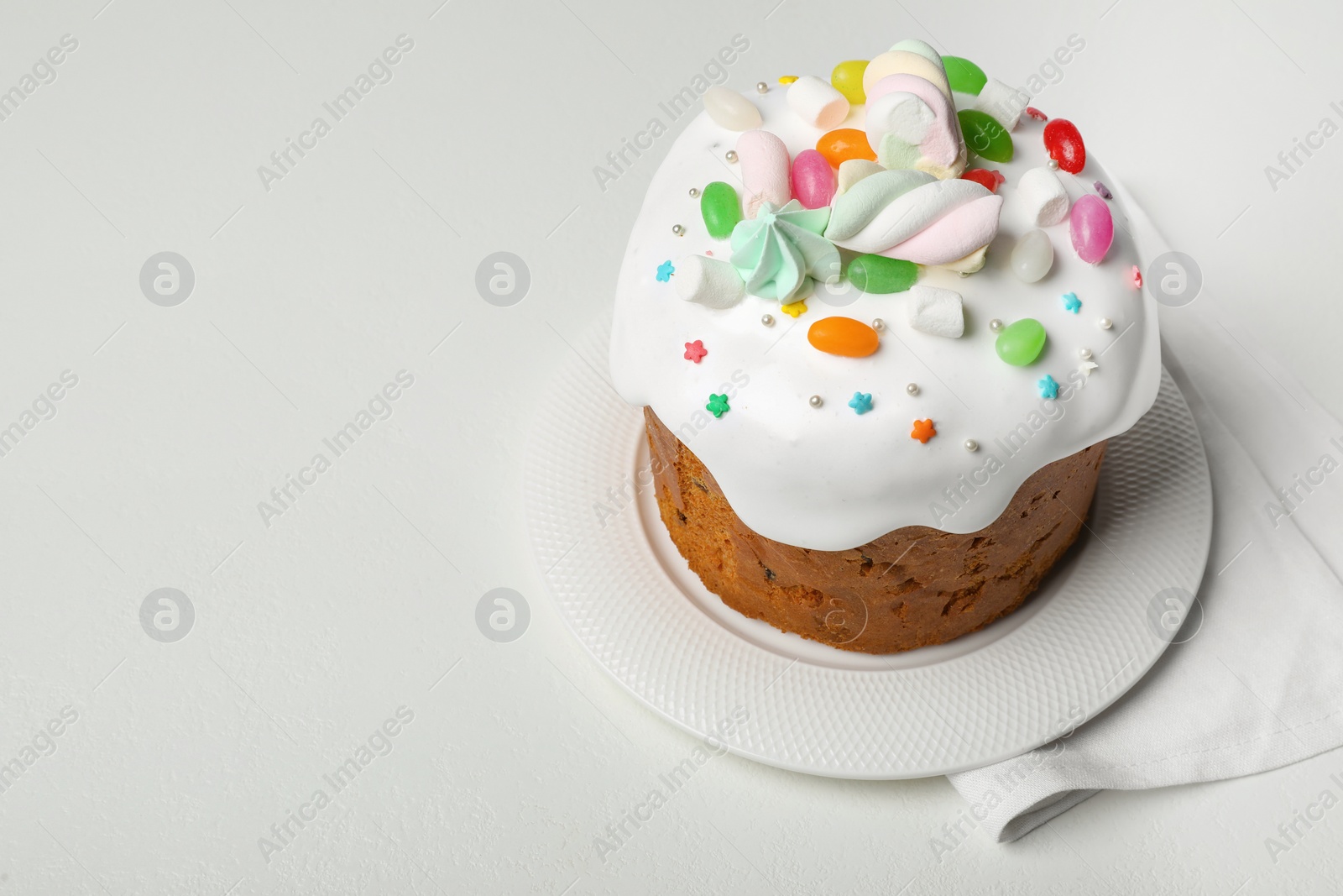 Photo of Traditional Easter cake decorated with sprinkles, jelly beans and marshmallows on white table, space for text