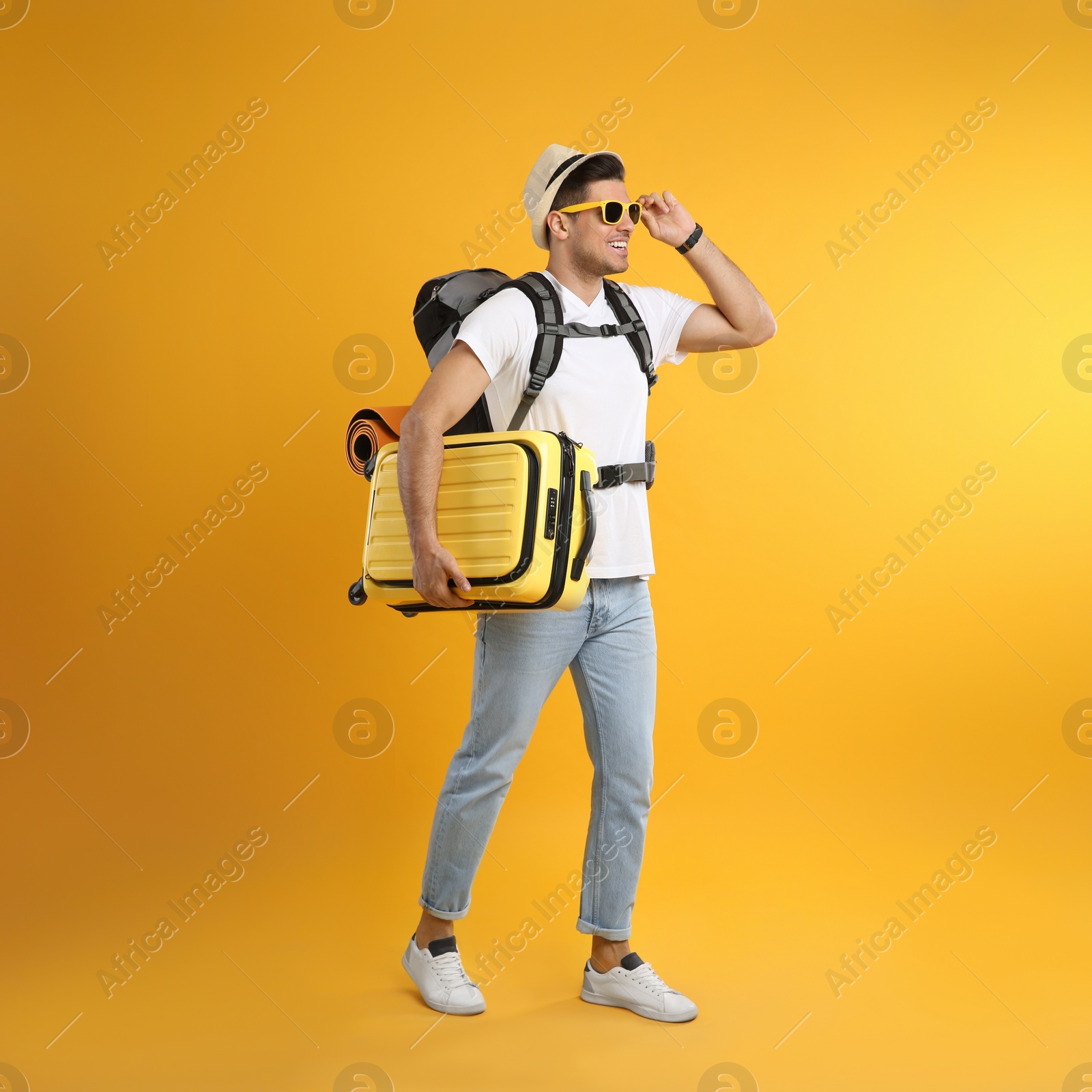 Photo of Male tourist with travel backpack and suitcase on yellow background