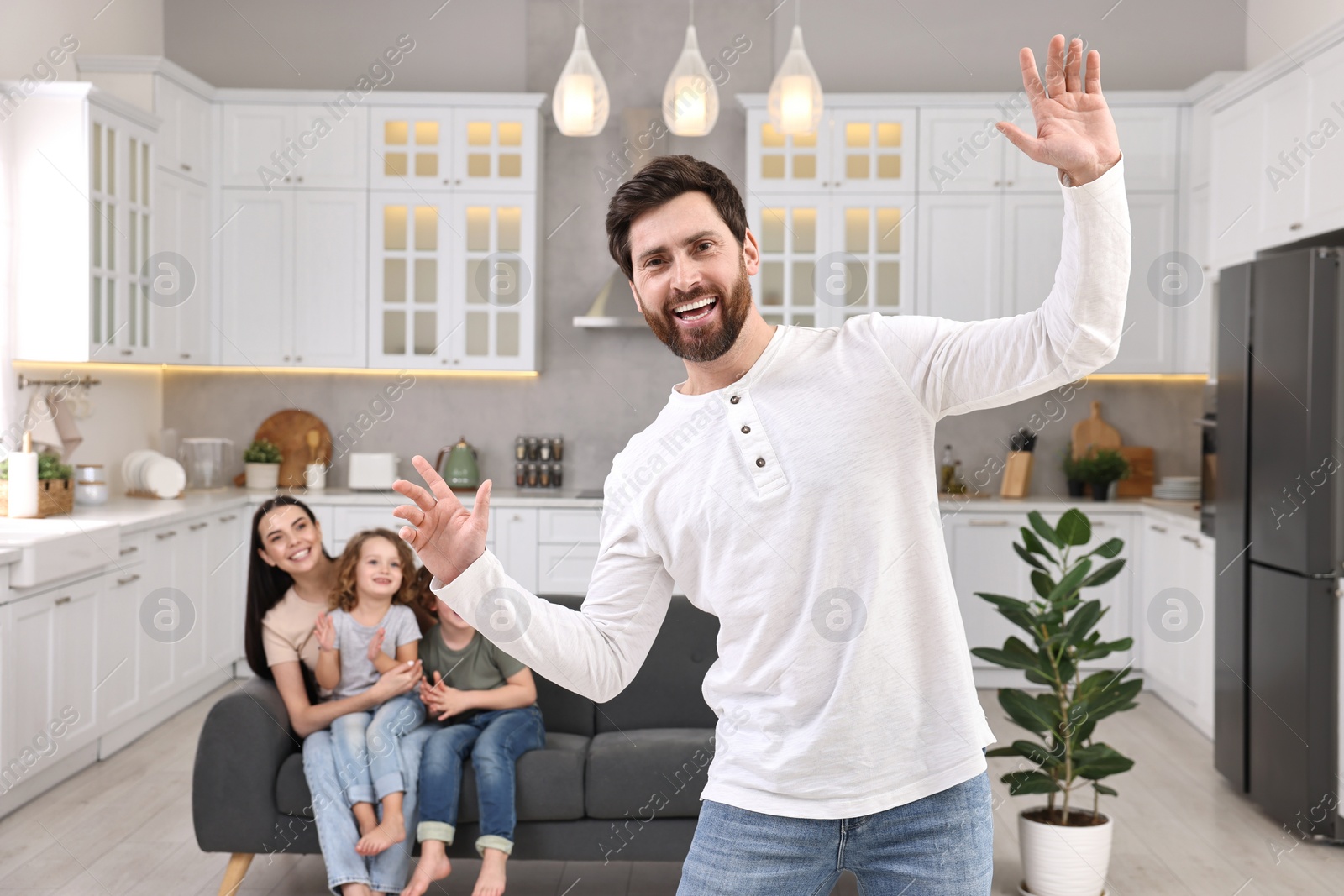 Photo of Happy family having fun at home. Father dancing while his relatives resting on sofa