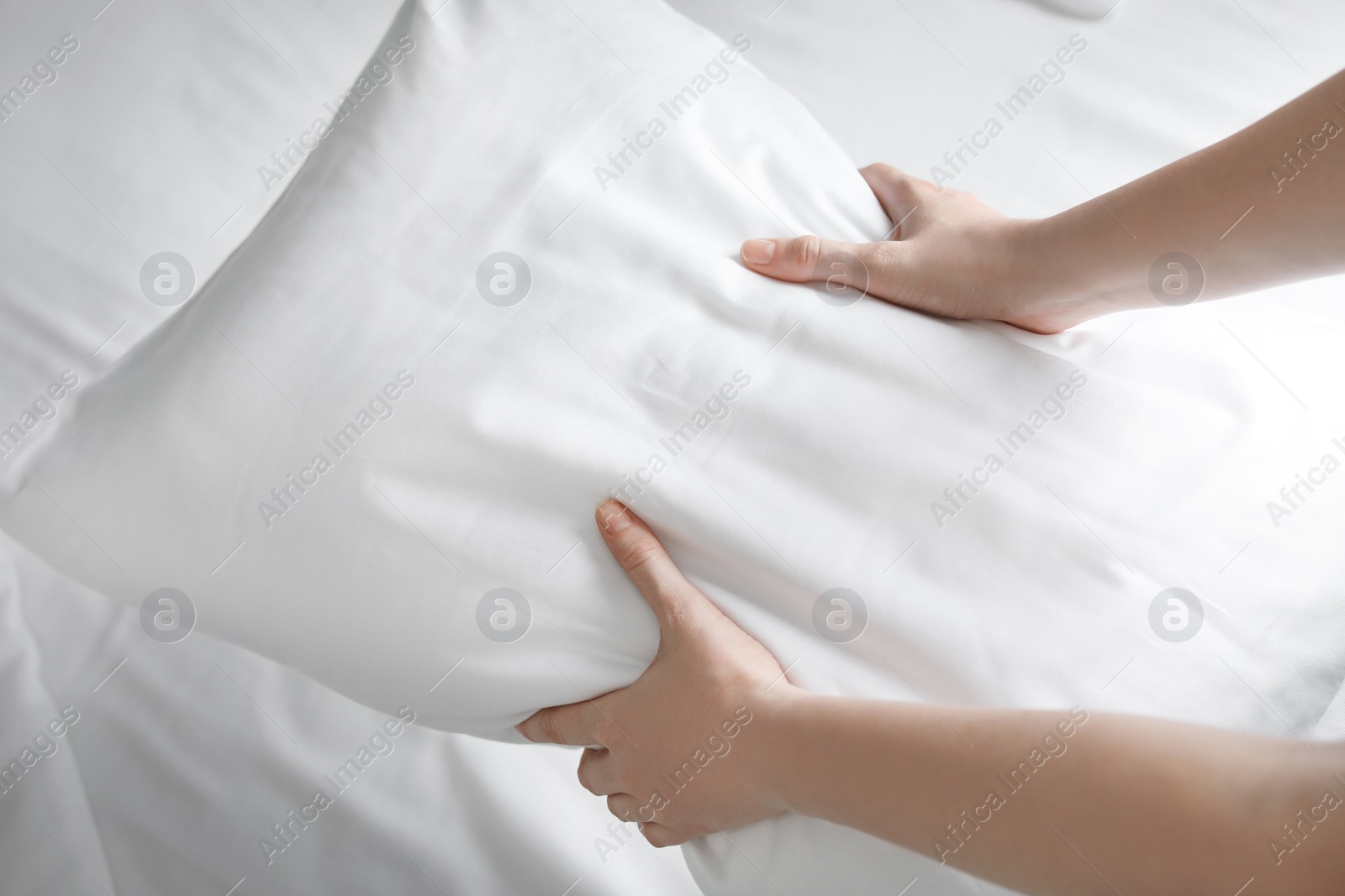 Photo of Young woman holding white pillow over bed, closeup