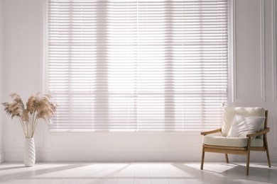Photo of Cosy armchair and decor near large window with blinds in spacious room. Interior design