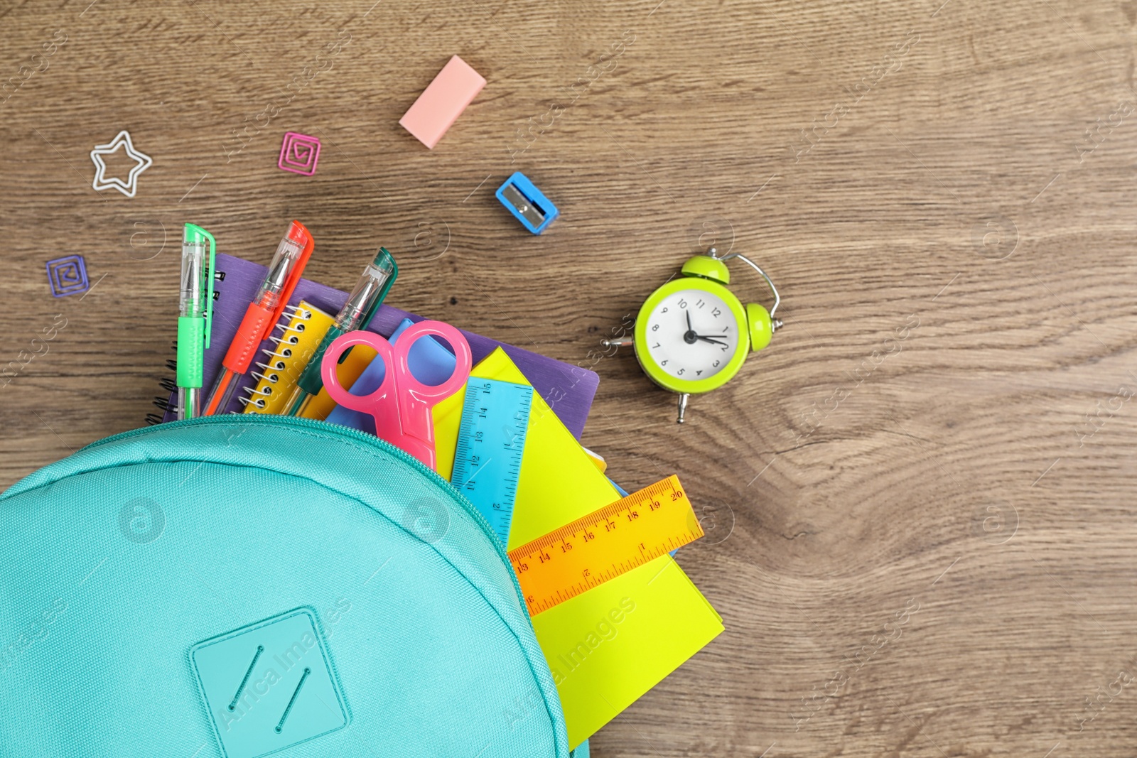 Photo of Stylish backpack with different school stationary and alarm clock on wooden table, flat lay. Space for text