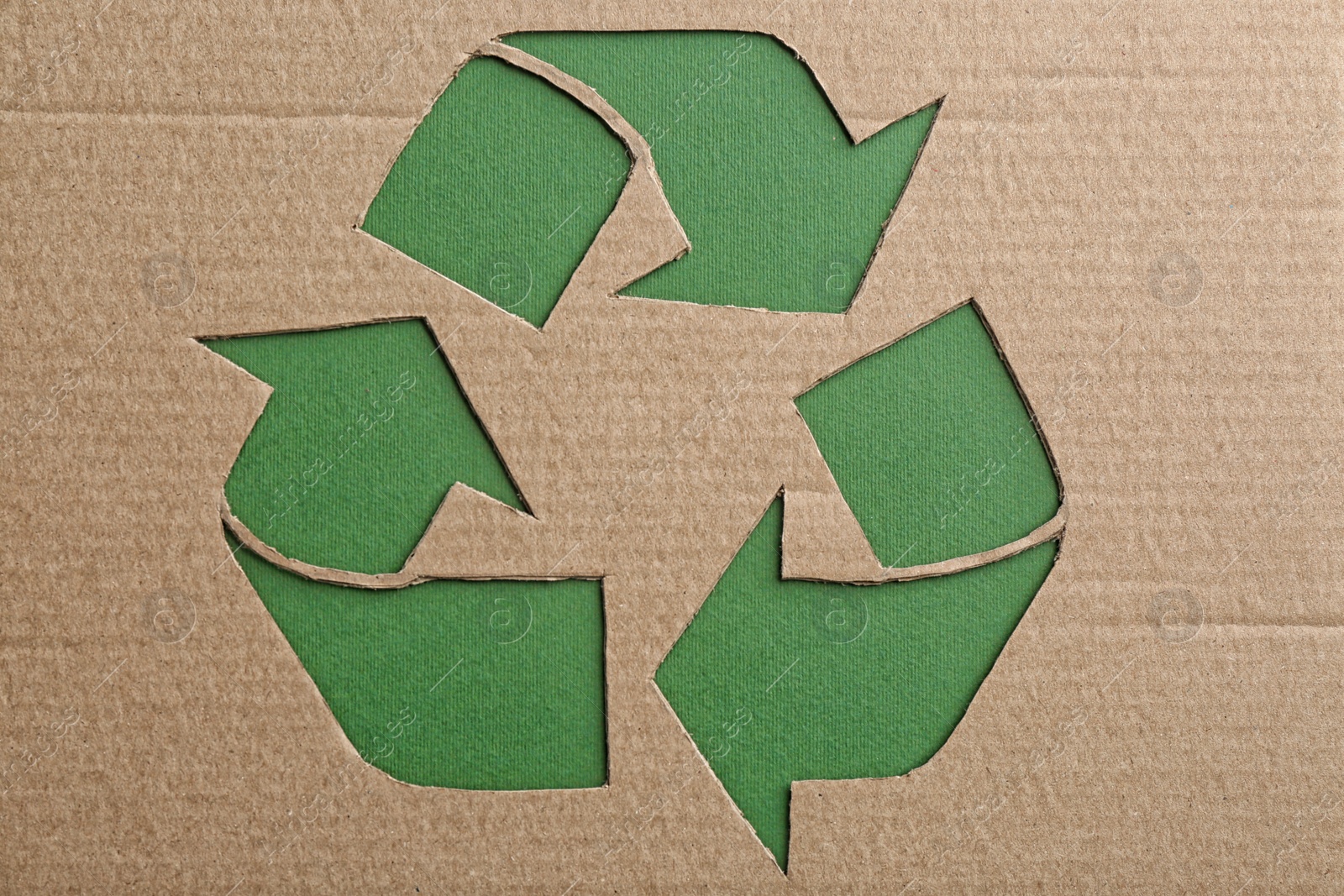 Photo of Sheet of cardboard with cutout recycling symbol on green background, top view