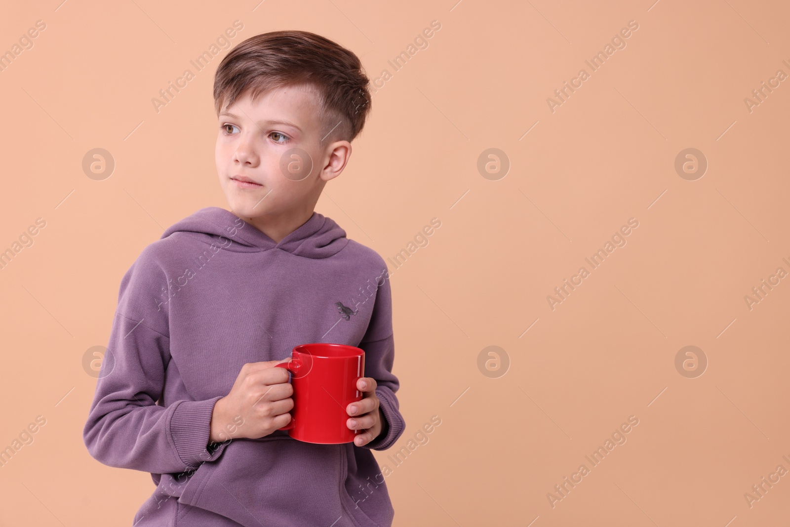 Photo of Cute boy with red ceramic mug on beige background, space for text