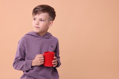 Cute boy with red ceramic mug on beige background, space for text