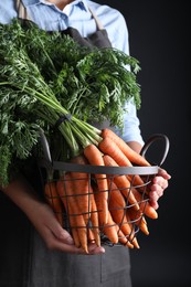 Woman holding basket with ripe carrots on black background, closeup