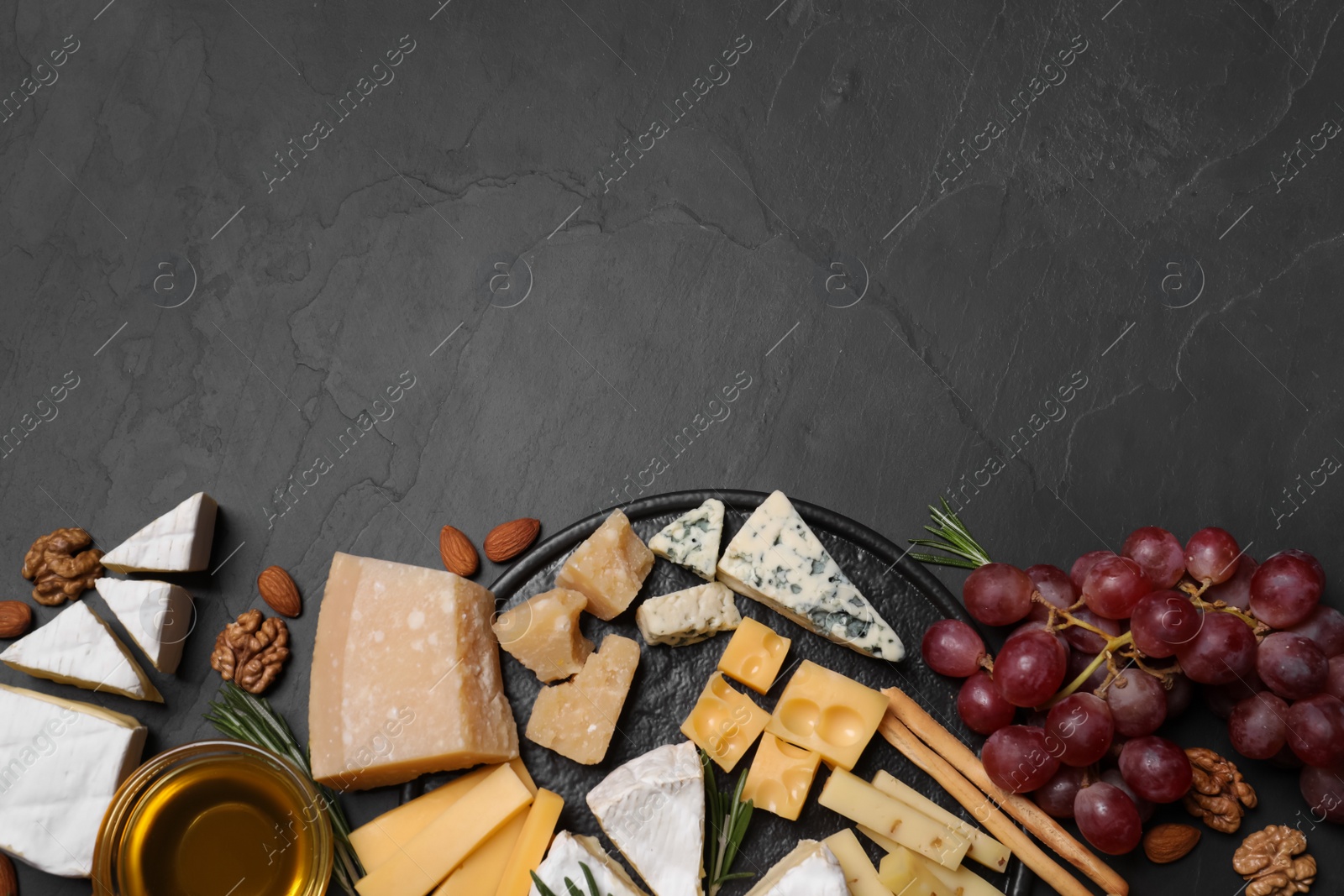 Photo of Cheese plate with honey, grapes and nuts on black table, flat lay. Space for text