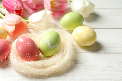 Photo of Sisal nest and painted Easter eggs on wooden table, space for text