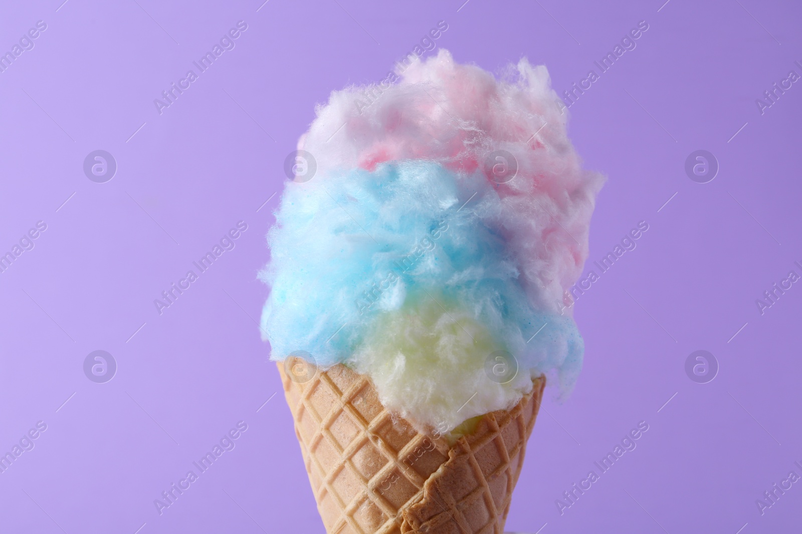 Photo of Sweet cotton candy in waffle cone on purple background, closeup