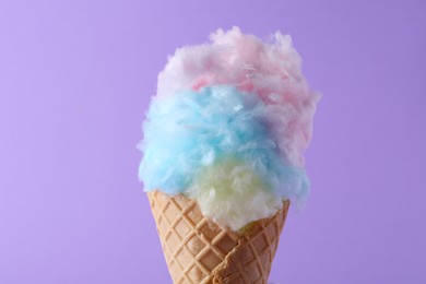 Photo of Sweet cotton candy in waffle cone on purple background, closeup