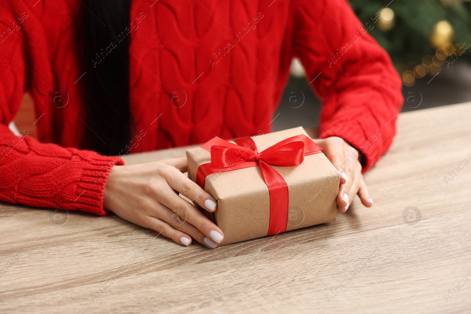 Photo of Woman with Christmas gift box at wooden table indoors, closeup