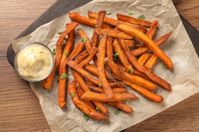 Photo of Board with delicious sweet potato fries and sauce on wooden table, top view
