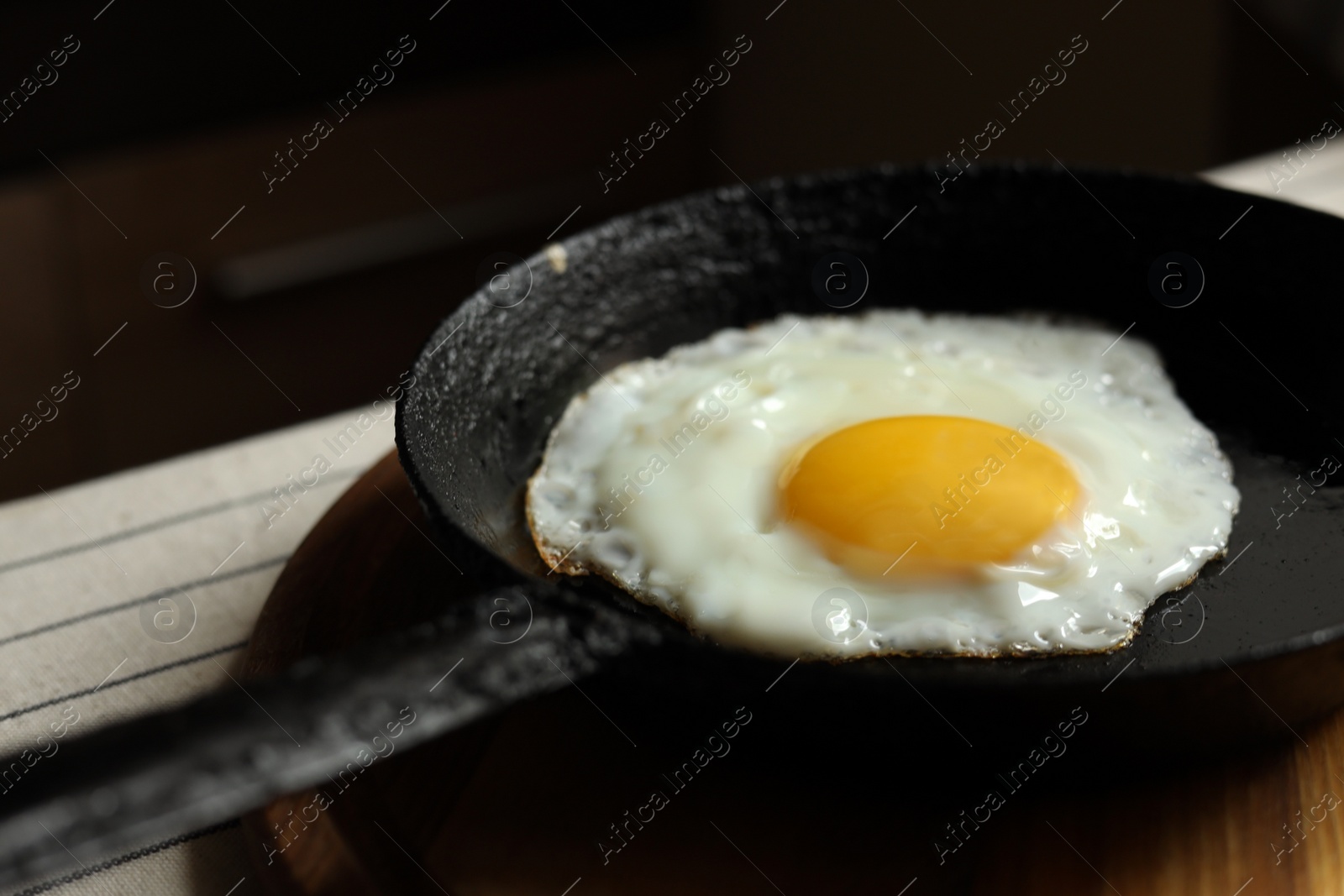 Photo of Frying pan with tasty cooked egg on wooden board, closeup