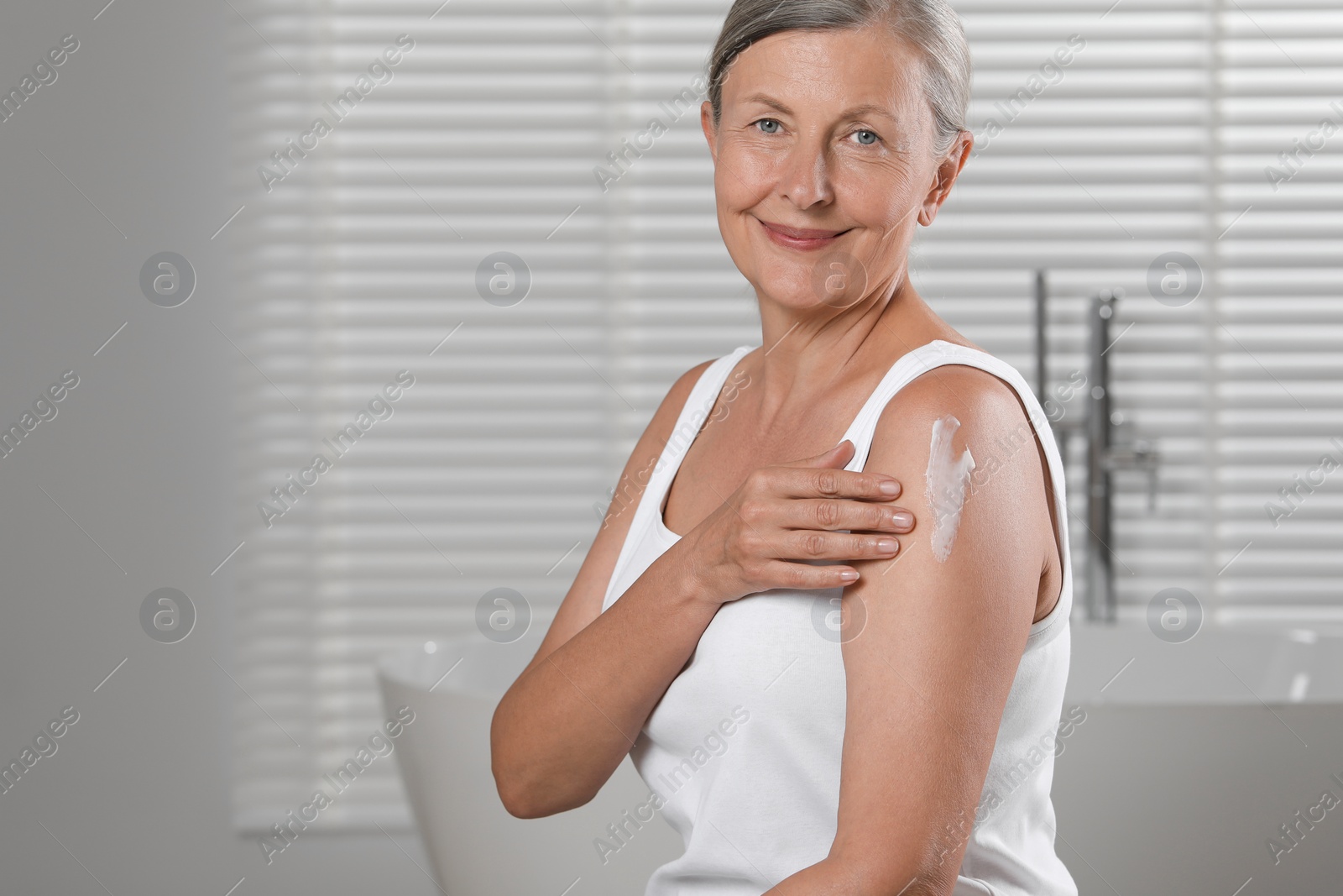 Photo of Happy woman applying body cream onto shoulder in bathroom. Space for text