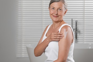 Happy woman applying body cream onto shoulder in bathroom. Space for text