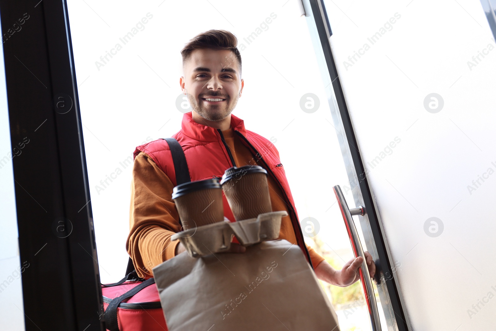 Photo of Portrait of courier with order at open door. Food delivery service