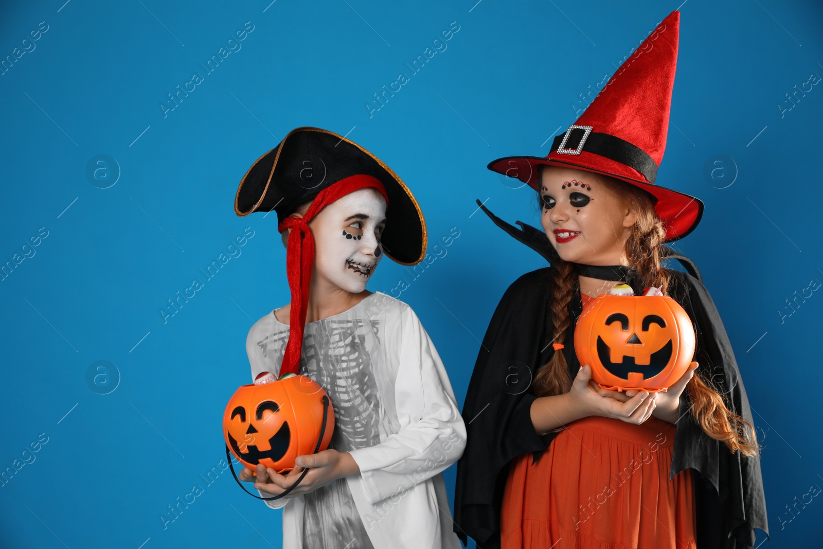 Photo of Cute little kids with pumpkin candy buckets wearing Halloween costumes on blue background