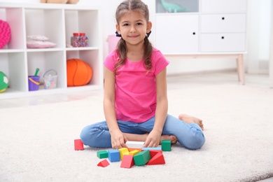 Photo of Cute child playing with colorful blocks on floor at home