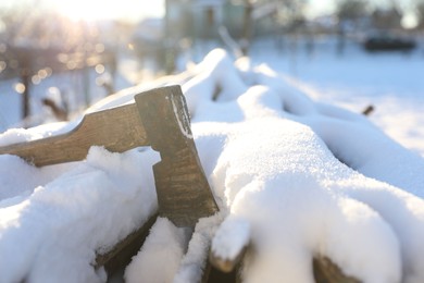 Metal axe on snowy firewood outdoors on sunny winter day