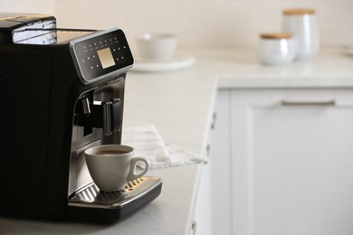 Photo of Modern electric espresso machine with cup of coffee on white marble countertop in kitchen